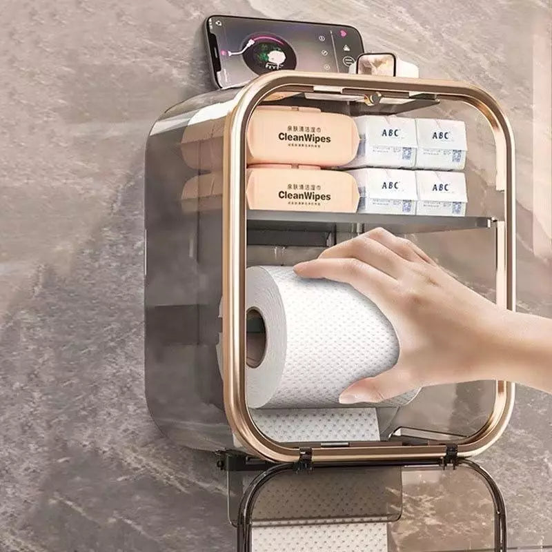 Mão puxando papel de caixa para banheiro; compartimentos para lenços e suporte de celular no topo.