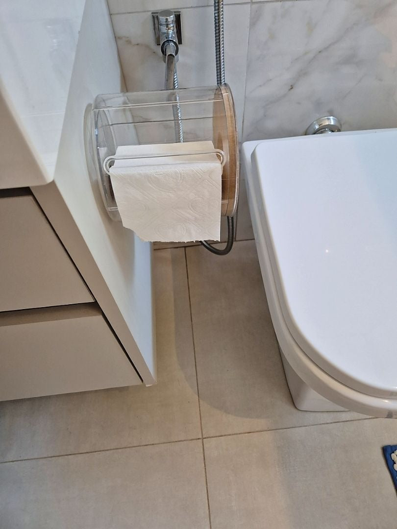 Porta papel higiênico transparente com tampa de bambu fixado próximo ao vaso sanitário no banheiro.