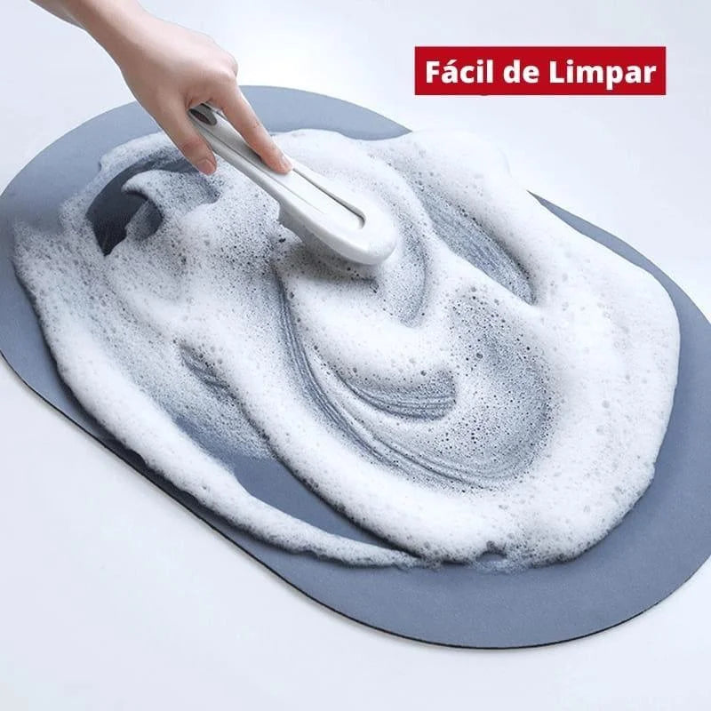 Tapete oval antiderrapante sendo limpo com espuma, de fácil limpeza e manutenção, destacando sua superfície impermeável e fácil manutenção.