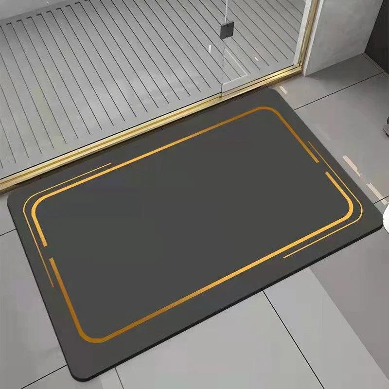 Tapete retangular preto com acabamento dourado, posicionado no chão do banheiro próximo ao box de vidro.